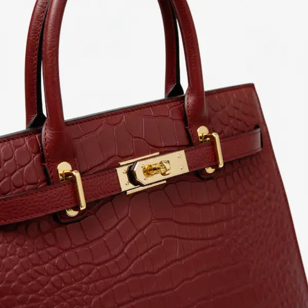 Close-up of Adara wine red leather satchel bag with embossed crocodile texture and gold clasp details