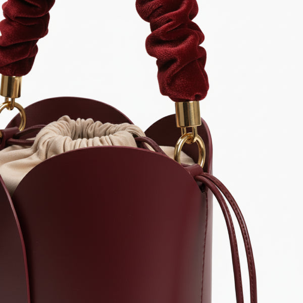 Althea Vegan Leather Bucket Bag in wine red, closeup highlighting ruched velvet handle, gold hardware, and beige drawstring pouch