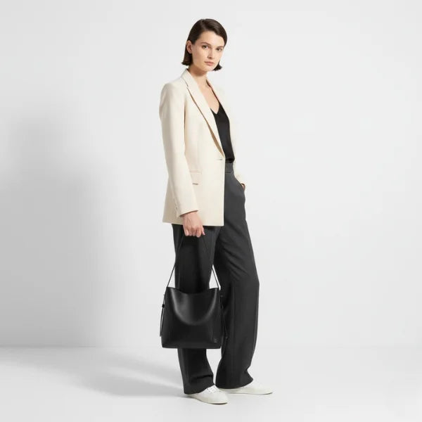 Amara Vegan Leather Bucket Bag in black, lifestyle studio shot with model in blazer and trousers holding the bag for scale and versatility