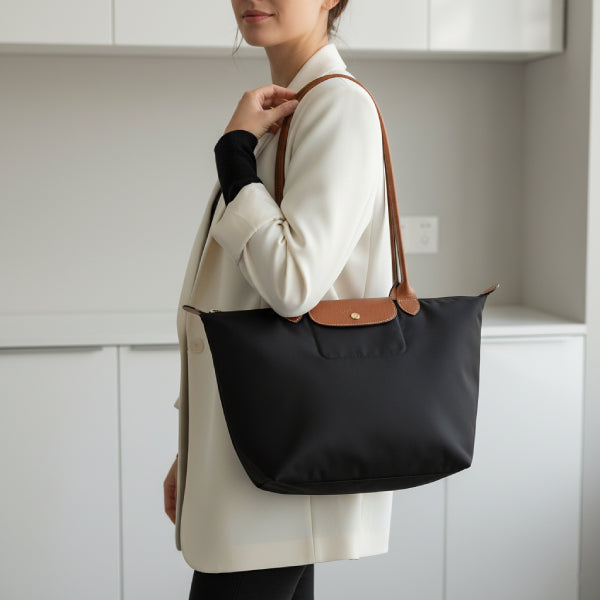 Model carrying Aria black vegan leather tote bag with brown leather handles in a modern indoor setting wearing a white blazer