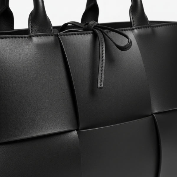Close-up of Aurelia black genuine leather tote bag showcasing the woven leather design and decorative tie closure