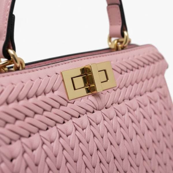 Close-up of pink woven vegan leather satchel bag with gold clasp and handle detail