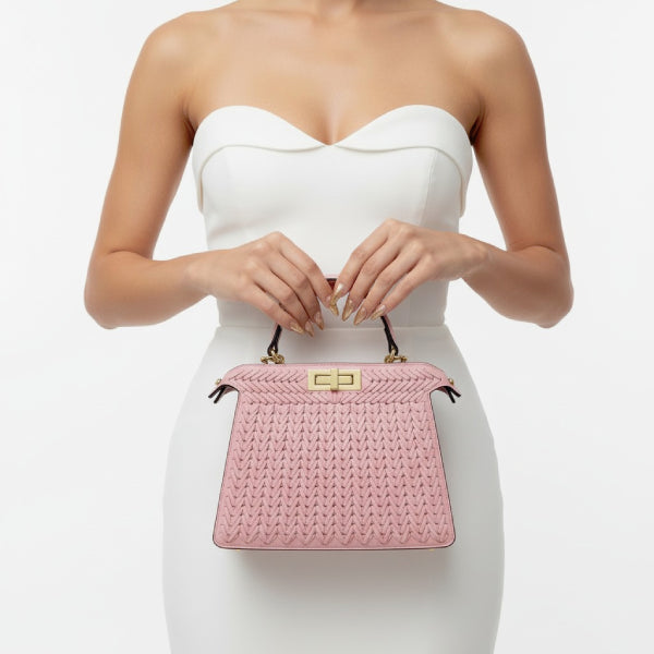 Model holding pink woven vegan leather satchel bag with gold clasp and handle, wearing a white dress