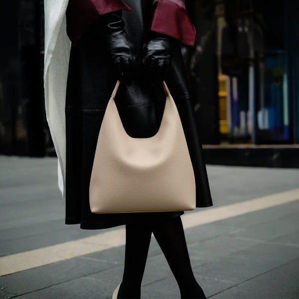 Model holding Elaria vegan leather hobo bag in off-white, styled with a minimalist design and adjustable strap