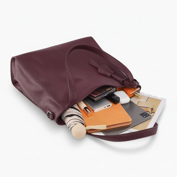 Close-up shot of a wine red vegan leather tote bag filled with various items such as a notebook, phone, and accessories, showing its spacious interior