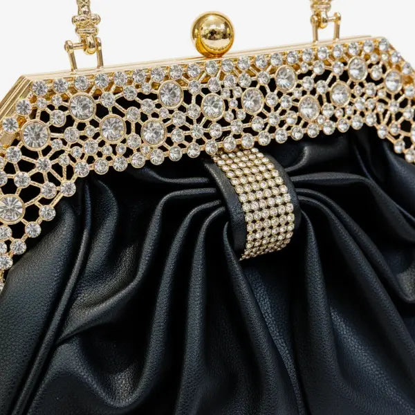 Close-up of a black vegan leather evening bag with a shiny gold frame and rhinestone-encrusted detailing