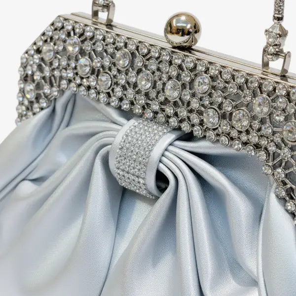Close-up of a blue vegan leather evening bag with rhinestone-encrusted gold frame and pleated satin finish