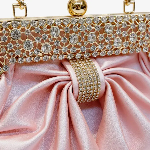 Close-up of a pink vegan leather evening bag with rhinestone-studded gold frame and pleated satin design