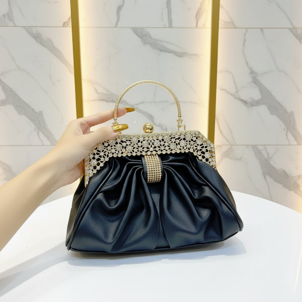 Handheld view of a black vegan leather evening bag with a golden frame and rhinestone embellishments, styled with a formal outfit