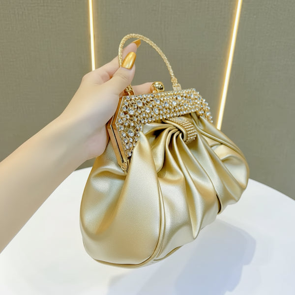 Handheld view of a gold vegan leather evening bag with rhinestone-encrusted gold frame and pleated satin fabric