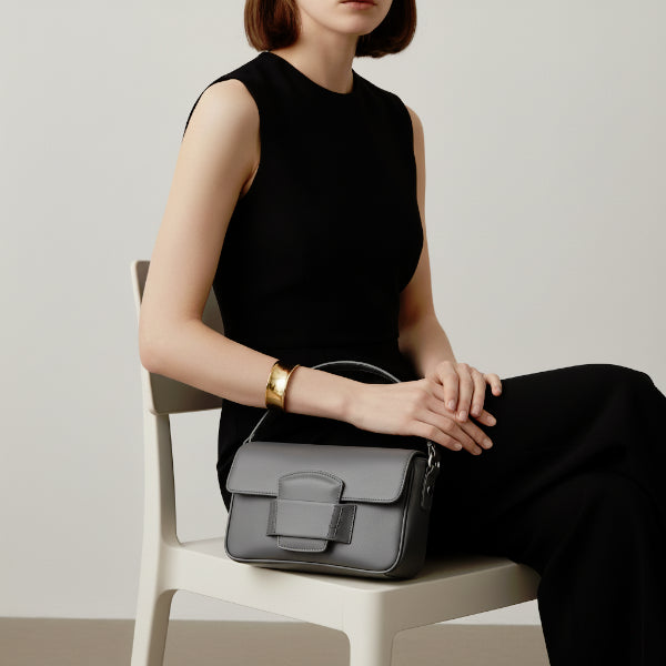 Faelina genuine cowhide shoulder bag in gray worn by model sitting, showcasing its elegant and functional design