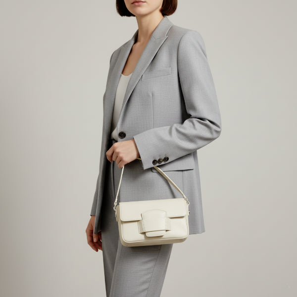 Faelina genuine cowhide shoulder bag in off-white worn by model in a sleek suit, highlighting its elegant and modern design