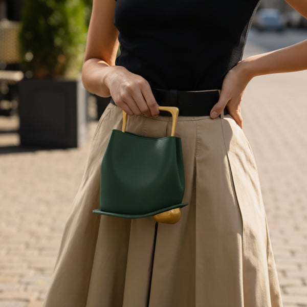 Izelia Genuine Leather Crossbody Bag in green, lifestyle street shot with model hand-carrying to show compact size and artistic base detail