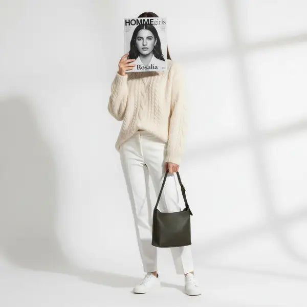 Model holding a black vegan leather shoulder bag while wearing a cream sweater and white pants