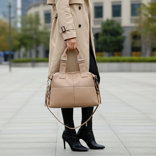 Model holding Mirelith khaki leather satchel bag with quilted handles, styled with a beige coat and black boots in an outdoor setting