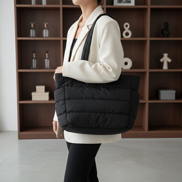 Model carrying a black puffer-style tote bag with quilted design, styled with a white blazer for a chic, urban appearance