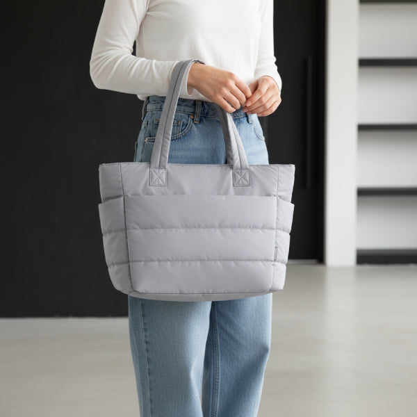 Model carrying grey puffer-style tote bag with quilted design, styled with a casual outfit, exuding modern elegance