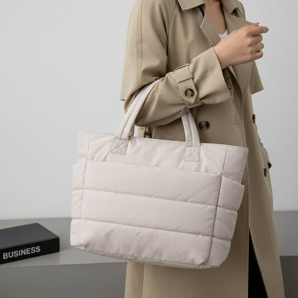 Model carrying off-white puffer-style tote bag, styled with a beige trench coat for a sophisticated and casual look