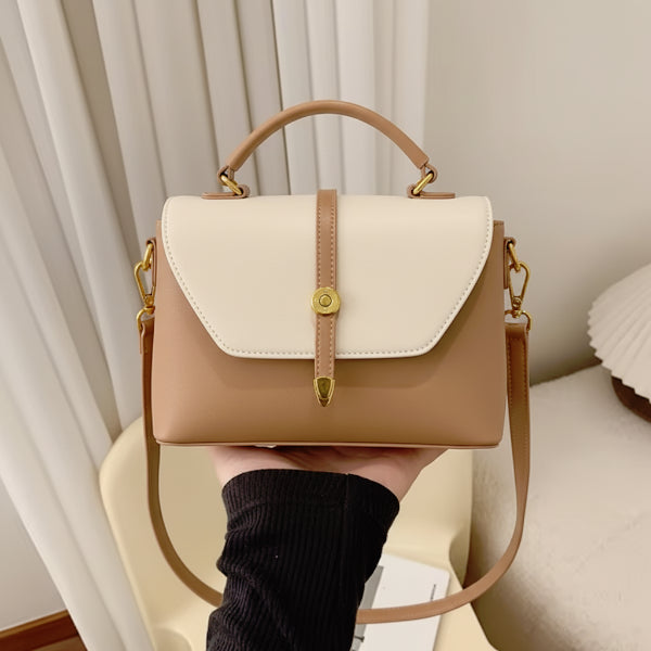 Handheld view of a beige vegan leather crossbody bag with a gold buckle detail