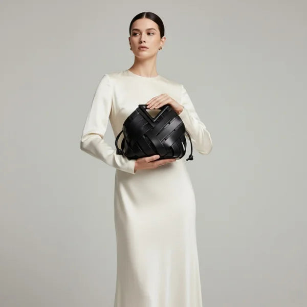 Seren Vegan Leather Bucket Bag in black, studio model holding the bag to showcase the statement triangular handle and woven design