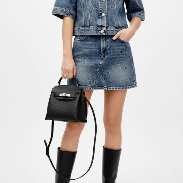 Female model wearing a denim skirt and jacket, holding a black genuine leather satchel bag with a silver clasp, ideal for casual yet fashionable outfits