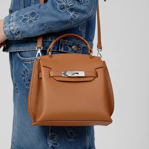 Female model wearing a denim outfit, carrying a brown genuine leather satchel bag with a silver clasp, perfect for casual yet chic looks