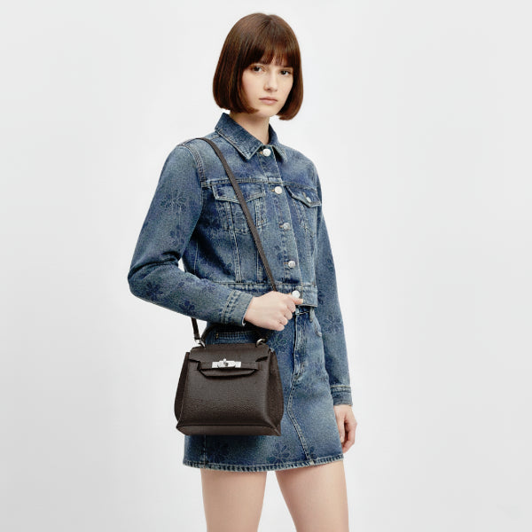 Female model in a denim outfit carrying a coffee brown genuine leather satchel bag with silver clasp, perfect for stylish daily wear