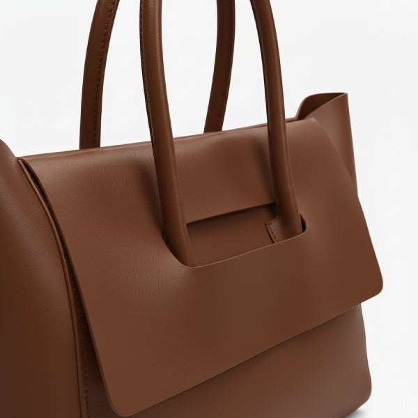 Close-up of brown vegan leather tote bag, showcasing its sleek design with a minimal flap closure and smooth finish