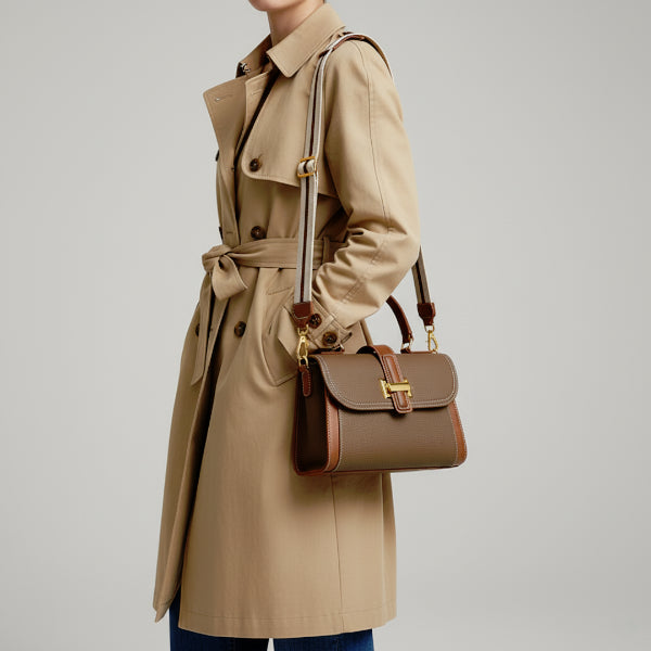 Model in a beige trench coat carrying a brown genuine leather satchel bag with gold-tone hardware, offering an elegant and timeless look