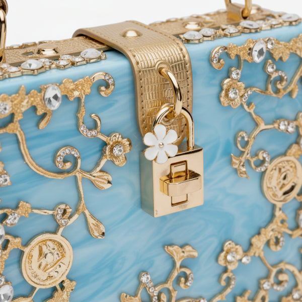 Close-up of Zephyra acrylic evening bag in blue with gold floral embellishments and lock clasp