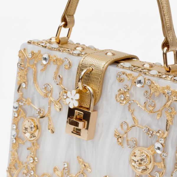 Close-up of Zephyra acrylic evening bag in white with intricate gold floral design and lock clasp
