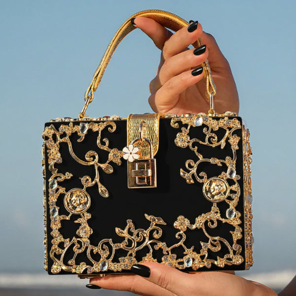 Handheld Zephyra acrylic evening bag in black with gold floral design and lock closure