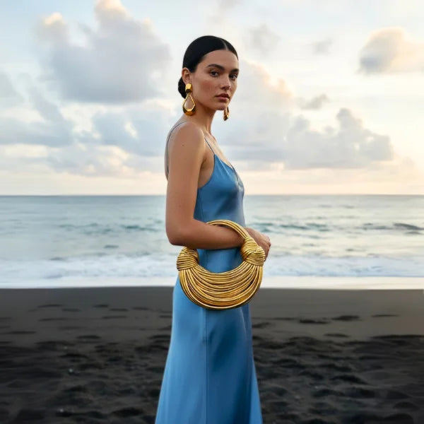 Zyra Vegan Leather Evening Bag in gold, lifestyle beach shot with model in satin dress highlighting bold sculptural design