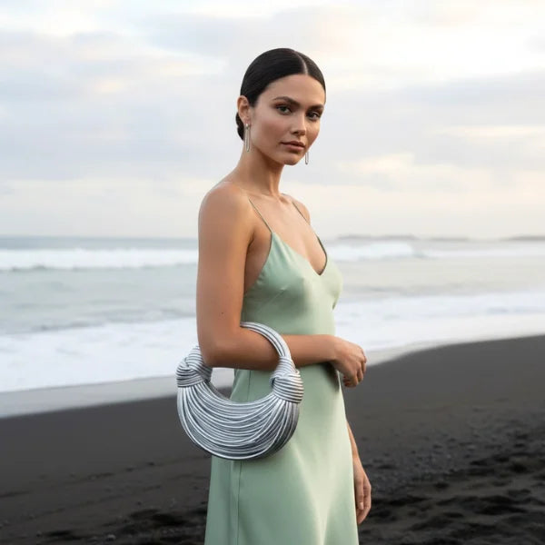 Zyra Vegan Leather Evening Bag in silver, lifestyle beach shot with model highlighting bold sculptural design and modern shine