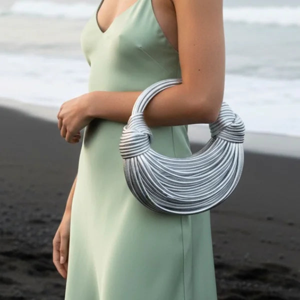 Zyra Vegan Leather Evening Bag in silver, lifestyle seaside shot with model showing arm carry and statement crescent shape