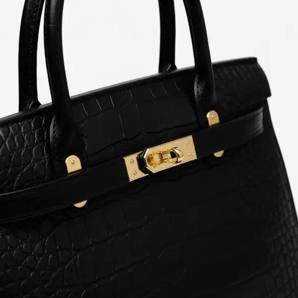 Close-up of Adara black leather satchel bag featuring gold clasp and embossed crocodile texture