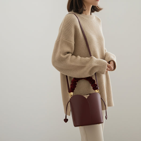 Althea Vegan Leather Bucket Bag in wine red, lifestyle shot with model wearing crossbody showing ruched velvet handle and heart-tipped drawstrings