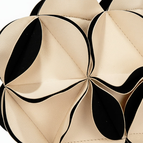Close-up of a beige vegan leather evening bag with geometric pleats in cream and black creating a flower-like pattern