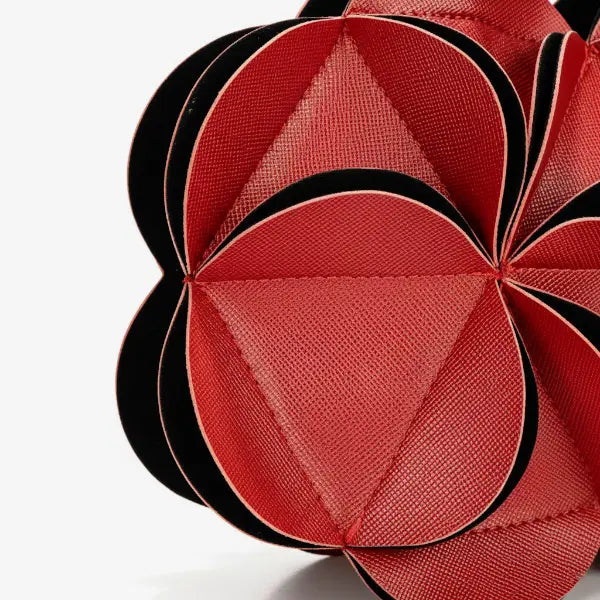 Close-up of a red vegan leather evening bag showcasing the intricate pleated flower pattern with black accents