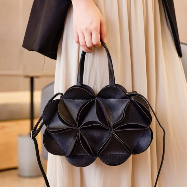 Model holding a black vegan leather evening bag with a flower-like geometric design and top handles