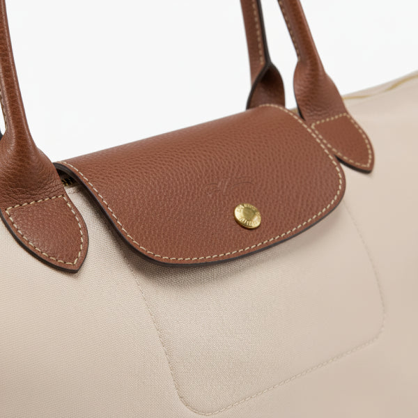 Close-up of Aria beige vegan leather tote bag showing the brown leather flap, button closure, and detailed stitching