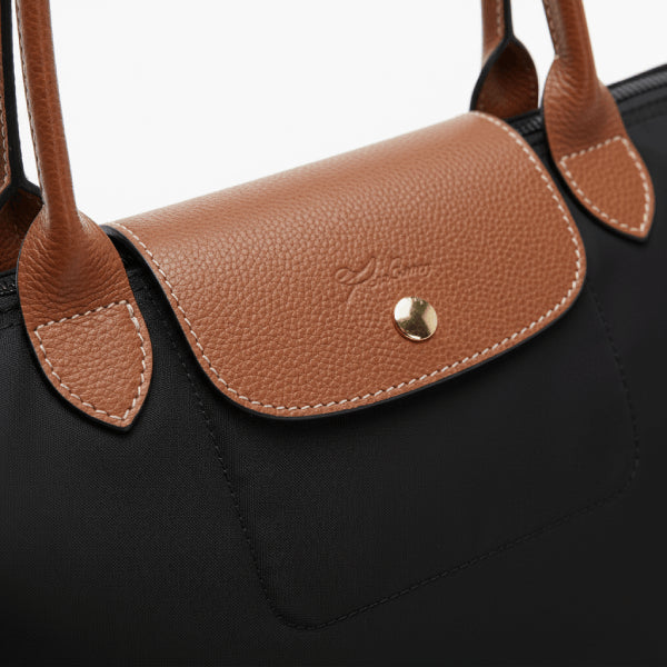 Close-up of Aria black vegan leather tote bag showcasing the brown leather flap with button closure and fine stitching