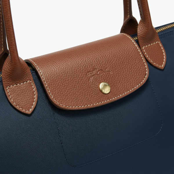 Close-up of Aria navy blue vegan leather tote bag featuring brown leather flap with button closure and stitching details