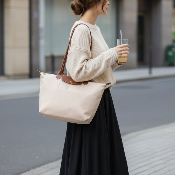 Model wearing Aria beige vegan leather tote bag with brown leather handles, holding a drink while walking on a city street