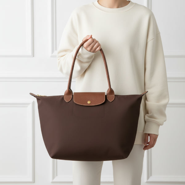 Model holding Aria brown vegan leather tote bag with brown leather handles, dressed in a white sweatshirt in a bright indoor setting