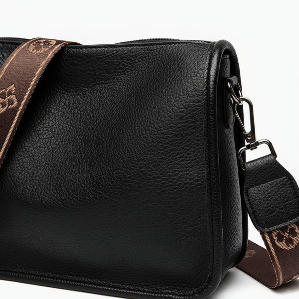 Auralis Genuine Cowhide Crossbody Bag in black, closeup of pebbled leather with silver hardware and wide brown jacquard shoulder strap