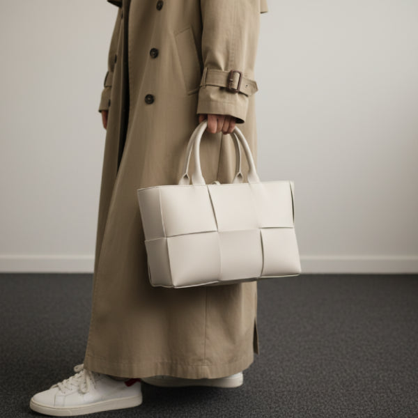 Model carrying Aurelia off-white genuine leather tote bag with a stylish woven design, dressed in a beige trench coat and sneakers