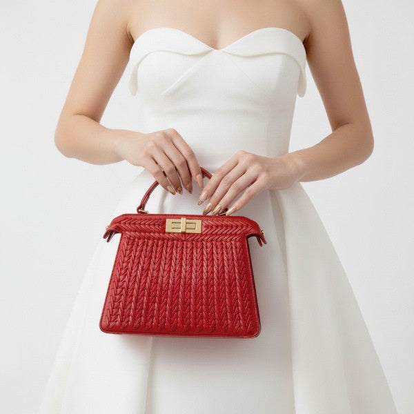 Model holding red woven vegan leather satchel bag with gold clasp and handle, wearing a white dress