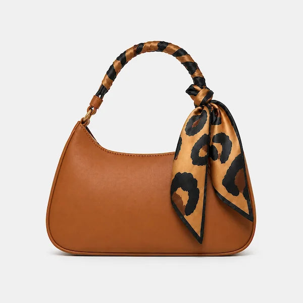 A brown leather shoulder bag with a curved top handle and a matching leopard-print silk scarf tied to the handle, shown against a light gray background.