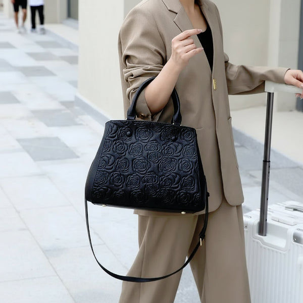 Model holding Azura genuine leather black satchel bag while wearing a beige suit in an outdoor setting